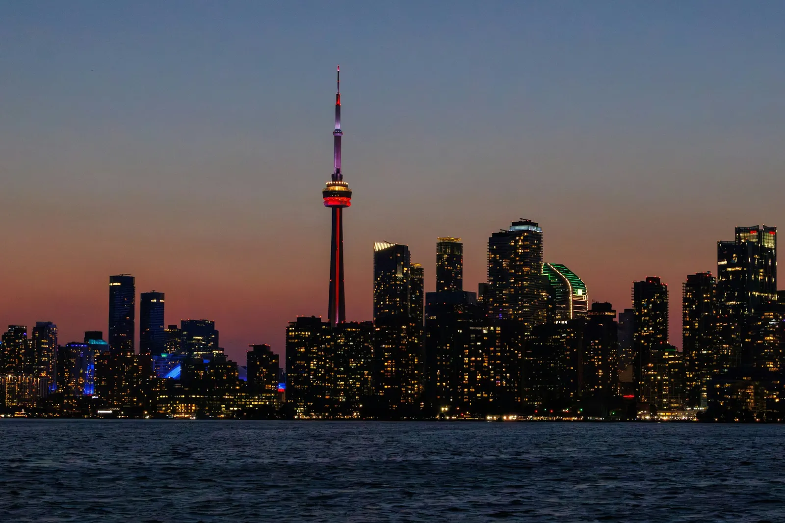 Toronto’s waterfront skyline at dusk, with the CN Tower above the illuminated buildings.
