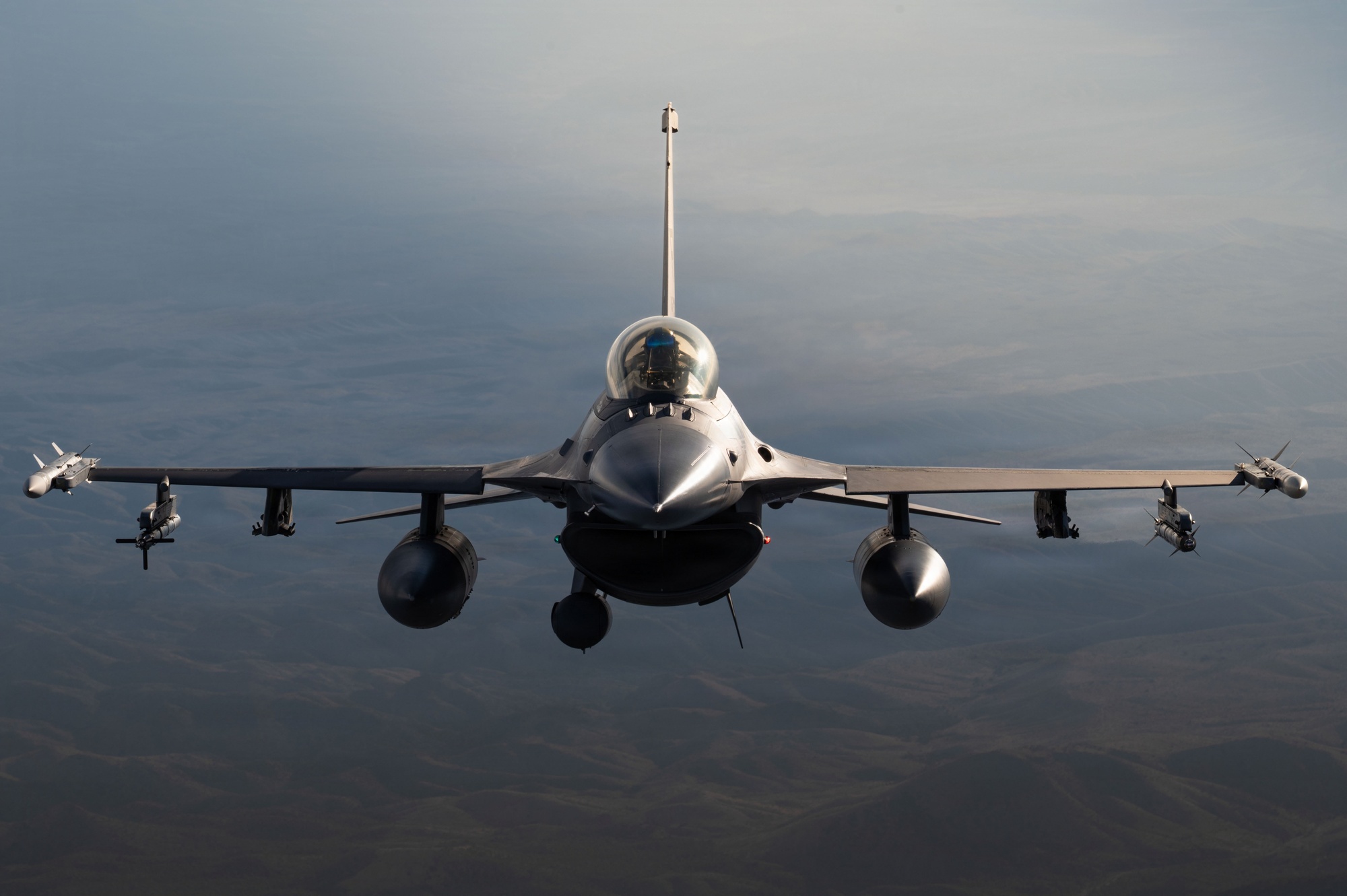 An F-16 Fighting Falcon flying head-on against a mountain landscape.